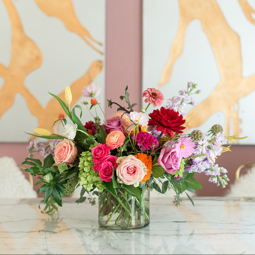 Red Dahlia, orange,ranunculus, orange zinnia arranged in a short clear glass vase, as captured in the studio of a Memphis, TN-based boutique floral design studio. The perfect choice for a romantic and timeless wedding