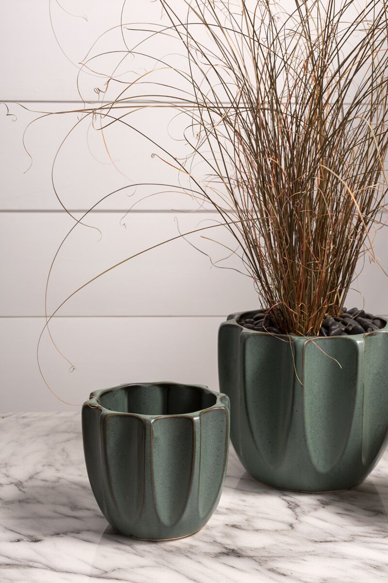 Two green ceramic planters with dried plants on a marble surface.