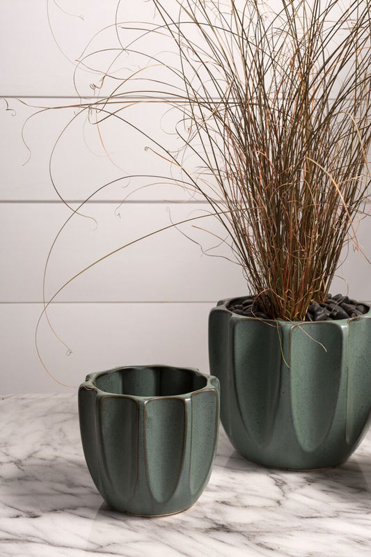 Two green ceramic planters with dried plants on a marble surface.