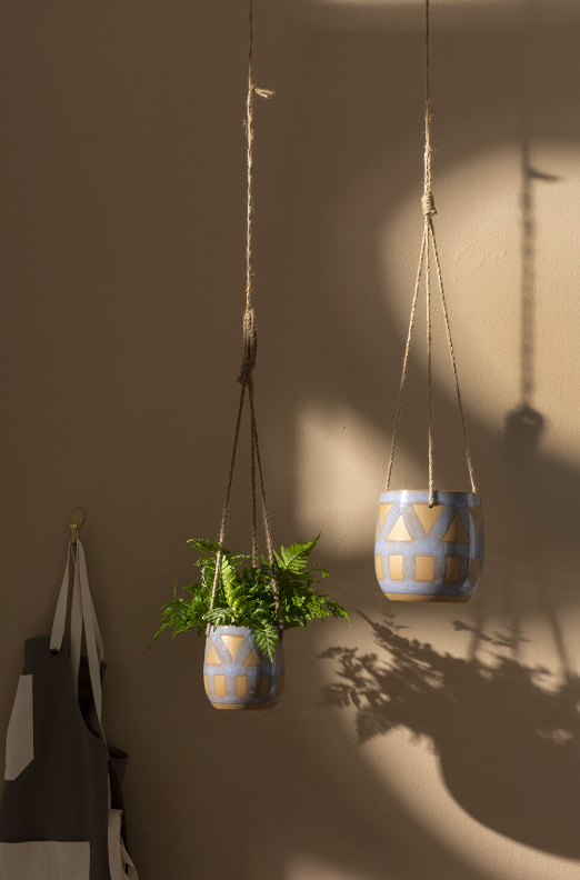 Two hanging planters with geometric patterns on a plain wall.