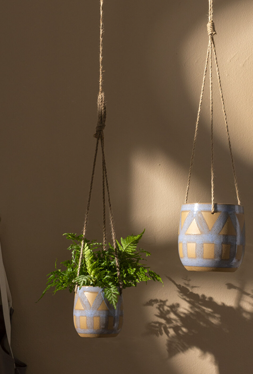 Two hanging planters with plants against a plain wall