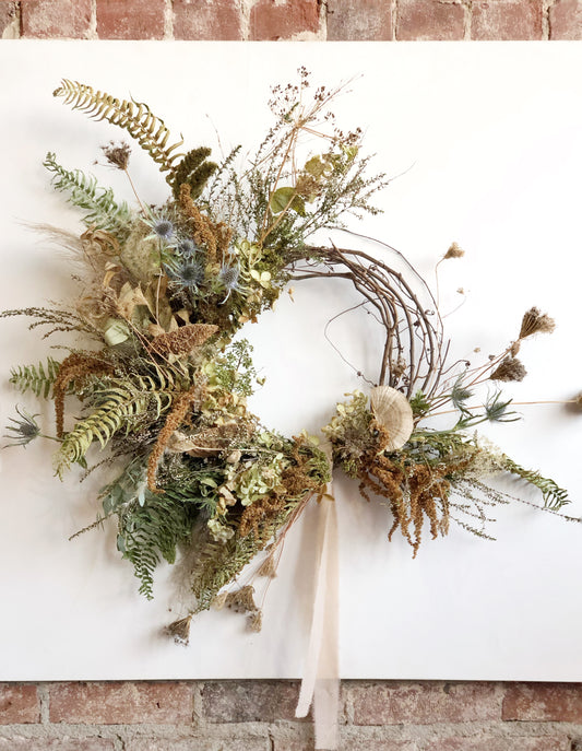Decorative wreath with greenery and a white ribbon on a brick wall background