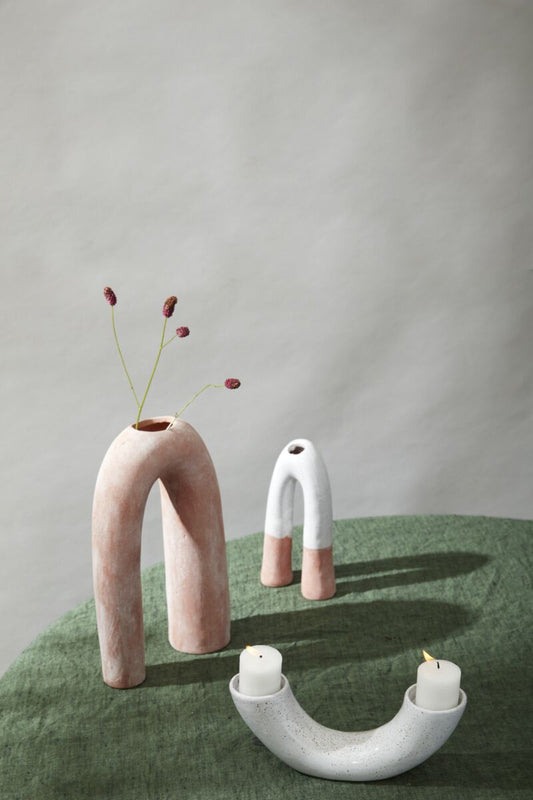 Set of ceramic arch-shaped vases and candle holders on a green surface with a neutral background