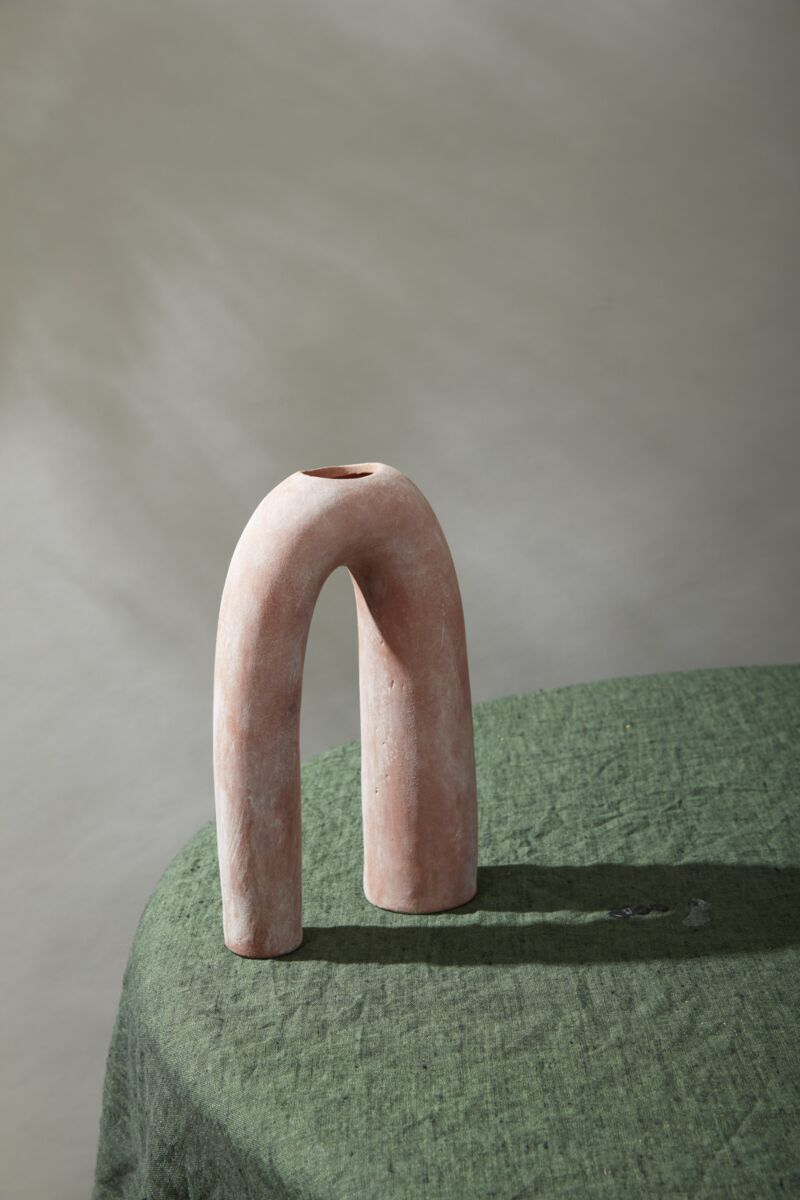 terracotta ceramic arch-shaped vase on a green surface with a neutral background