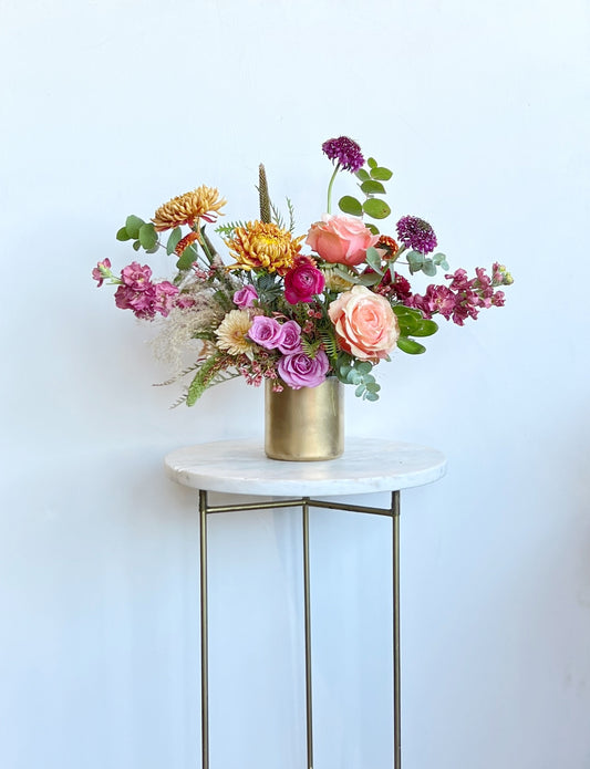 Colorful flower arrangement in a gold vase on a marble table against a light blue background